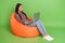 Portrait of attractive cheerful skilled girl sitting in chair using laptop web university isolated over bright green
