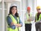 Portrait of attractive confident female construction worker standing with arm crossed at construction site with two male engineer