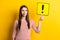 Portrait of attractive doubtful girl holding exclamation point card deciding isolated over bright yellow color