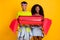 Portrait of attractive funky cheerful couple holding in hands large fake candy having fun isolated on bright yellow