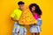 Portrait of attractive funky cheerful couple holding large fake pizza biting isolated on bright yellow color background