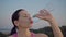 Portrait of an attractive girl on the background of the city. Sportswoman in a purple t-shirt drinks water from a bottle