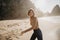 Portrait of attractive girl with light brown hair running on rocky Ursa beach on sunset. Smiling looking to the camera