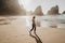 Portrait of attractive girl with light brown hair walking on rocky Ursa beach on sunset. back view