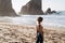 Portrait of attractive girl with light brown hair walking on rocky Ursa beach on sunset. back view