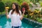 Portrait of attractive girl with mango and dragon fruit, pitaya in her hands standing in tropical garden with pool