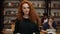 Portrait of an attractive long red haired european girl student standing in high school library smiling looking at
