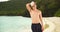 Portrait of attractive man standing shirtless in swim shorts on Caribbean beach.
