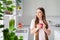 Portrait of attractive minded dreamy long-haired girl drinking latte cacao resting in light white home kitchen indoors