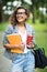 Portrait of attractive mixed race woman student in eyesglasses with coffee to go and textbook in hands and looking at camera