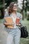 Portrait of attractive mixed race woman student in eyesglasses with coffee to go and textbook in hands and looking at camera