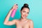 Portrait of attractive naked cheerful girl using modern spray making coiffure prepare  over bright teal