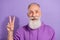 Portrait of attractive optimistic cheerful grey-haired man showing v-sign isolated over purple violet color background