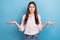 Portrait of attractive puzzled brown haired girl shrugging shoulders isolated over bright blue color background