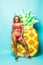 Portrait of attractive slim body woman in red bikini and sunglasses posing with pineapple inflatable mattress isolated on gre