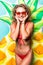 Portrait of attractive slim body woman in red bikini and sunglasses posing with pineapple inflatable mattress isolated on gre