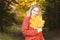 Portrait of an attractive smile young blonde in a red coat with a bouquet of yellow leaves in her hand. The concept of