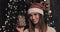 Portrait of attractive smiling young caucasian girl wearing santas hat standing near the christmas tree at cosy