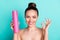 Portrait of attractive trendy naked cheerful girl holding spray showing ok-sign  over bright teal turquoise