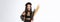 Portrait of attractive woman in witch costume celebrating halloween, pointing at broom, standing over white background