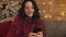 Portrait of attractive young brunette woman using her smartphone typing sitting near Christmas tree at grey sofa indoor