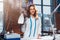 Portrait of attractive young Caucasian brunette dressmaker standing in white clothes holding steam iron in studio.