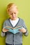 portrait of attractive young diligent little school boy reading a book over green background, isolated