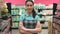 Portrait of attractive young saleswoman in apron standing in supermarket with her hands crossed, looking at camera and