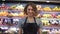 Portrait of attractive young saleswoman in black apron standing in supermarket with shelves of fruits on background