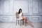 Portrait of attractive young woman sitting in a chair. elegant white dress. White floor and white wall in the background