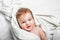 Portrait of baby 11 months old on bed close up. Funny kid on white cloth smiles. Restful sleep concept, teething, baby care.