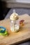 A portrait of a baby bottle with a bit of milk still in it standing on a wooden plank. The glass nursing bottle still has some
