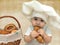 Portrait of a baby boy in a chefs hat with a basket of muffins and bagels