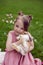 portrait baby girl in a pink dress plays with a rabbit in a green meadow in summer. Funny friendship between a child and