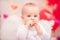Portrait of a baby girl with white feather wings eating heart-shaped cookies, symbols of Valentine`s Day