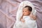 Portrait of baby infant covered with white cloth laying down on soft furry bed in studio.