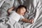 Portrait of baby in sleepwear lying under blanket on bed at home. Sleeping hands apart infant child in bedroom, see