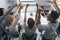 Portrait from back of glad students sitting together at the table and raising hands. Indoor photo of team of freelance