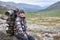 Portrait of backpacker enjoying on stone in mountain valley, tired man with backpack resting in mountains, copyspace