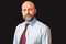 Portrait of a bald businessman in his 40s on a dark background. Slim male with grey beard and friendly face in light shirt and red