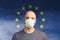 Portrait of a bald man in a respirator against the background of the flag of the European Union