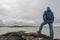 Portrait of bald man standing on a rock by the ocean, hands on his hips, back to camera, beautiful and calm scenery in the