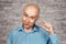 Portrait bald sad man thinks about money and a small salary. White bald guy in blue shirt on brick wall background showing thumbs