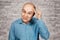 Portrait bald sad man thinks about money and a small salary. White bald guy in blue shirt on white brick wall background showing