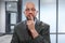 Portrait of a bald unshaven businessman in grey suit on blurred office background. Hand at his face