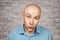 Portrait bald unsure man doesn`t understand anything . guy in a blue shirt on white brick wall background in perplexity