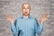 Portrait bald unsure man doesn`t understand anything and spreads his hands. guy in a blue shirt on white brick wall background in