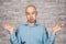 Portrait bald unsure man doesn`t understand anything and spreads his hands. guy in a blue shirt on white brick wall background in