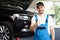 Portrait of bearded car mechanic in a car workshop shows thumbs up. Positive auto service worker in blue overalls and
