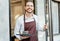 Portrait of bearded happy barista man working waitress in cafe open entrance door and serving drinks on a tray in front of the